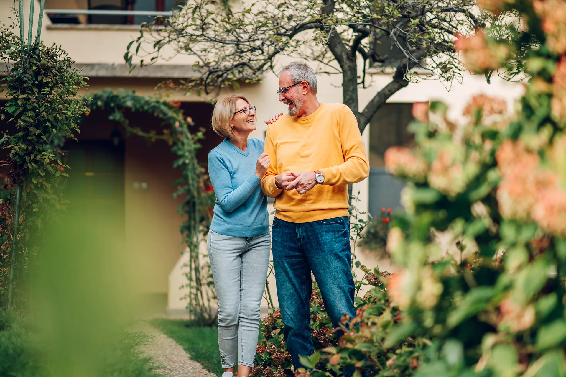 Glückliches älteres Paar spaziert durch ihren Garten vor dem Eigenheim
