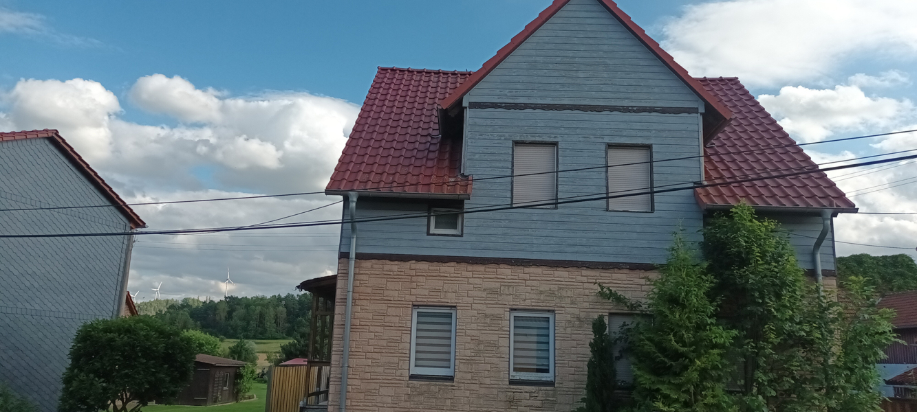 Vorderseite eines sanierungsbedürftigen Hauses mit Holzfassade und modernem Dach in ruhiger Lage von Ellrich-Gudersleben